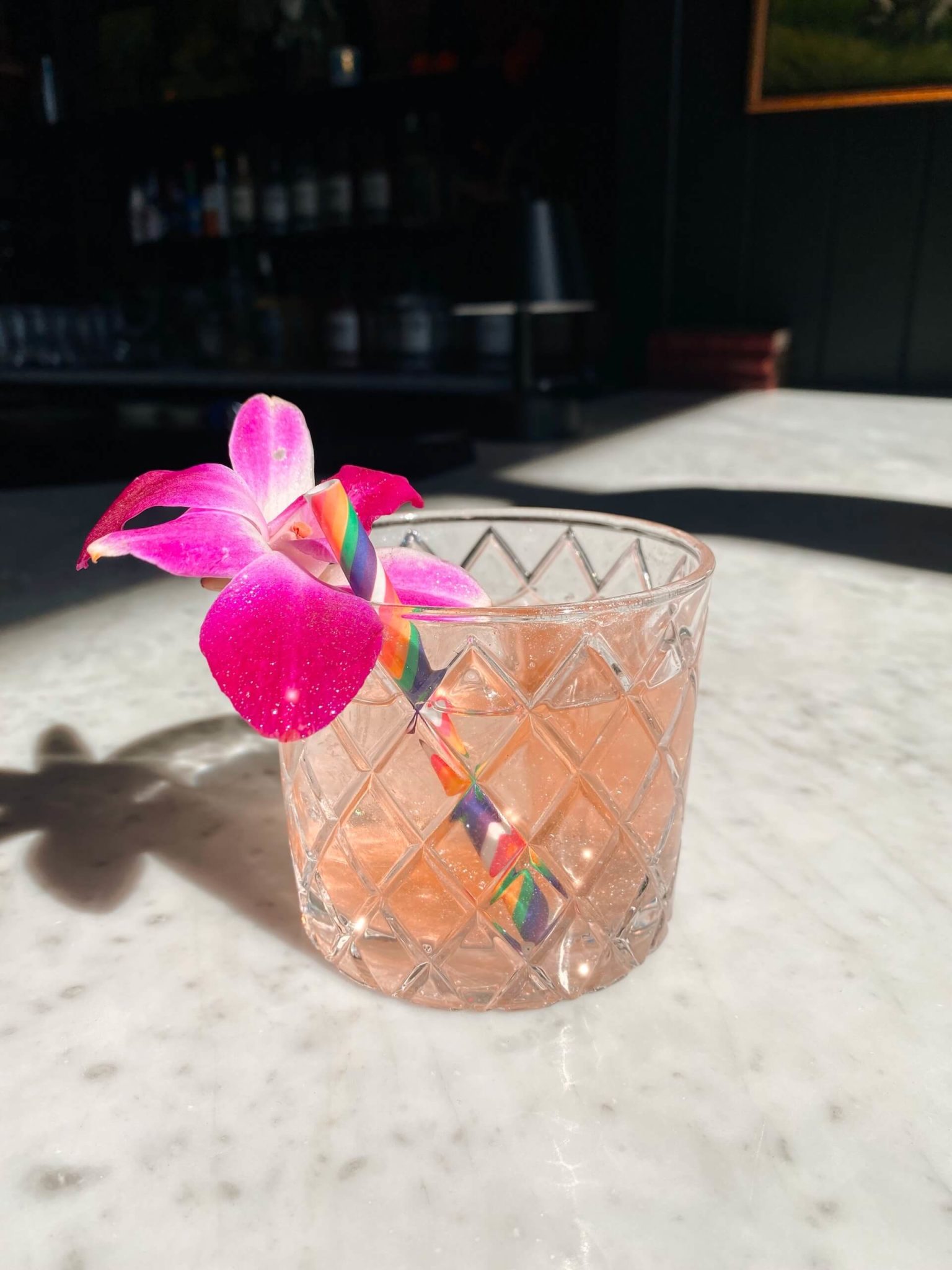 cocktail in rocks glass with sparkles, pink flower & rainbow straw